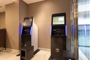 Two self-service kiosks in a hotel lobby with a modern design, a tiled floor, and a large window with blinds. - KEIKYU EX INN Higashiginza (Tokyo)