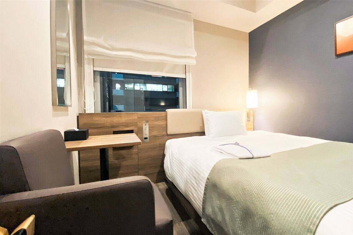 A hotel room with a bed, a desk, a chair, a window, and a wall-mounted picture.