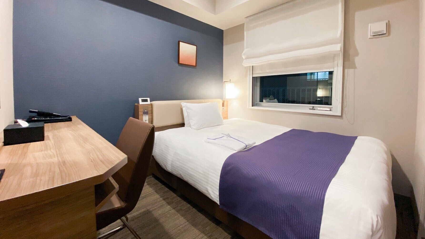 Une chambre d’hôtel avec un lit, une table de chevet, une chaise, une lampe et une fenêtre donnant sur un paysage agréable.