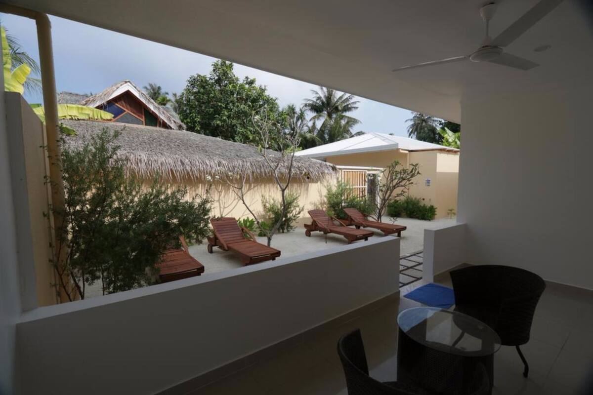 A balcony with wooden lounge chairs, a glass table, and a ceiling fan.