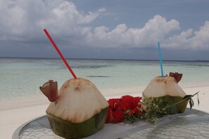 Two coconuts with straws on a table by the beach. - Scuba Inn (Omadhoo)
