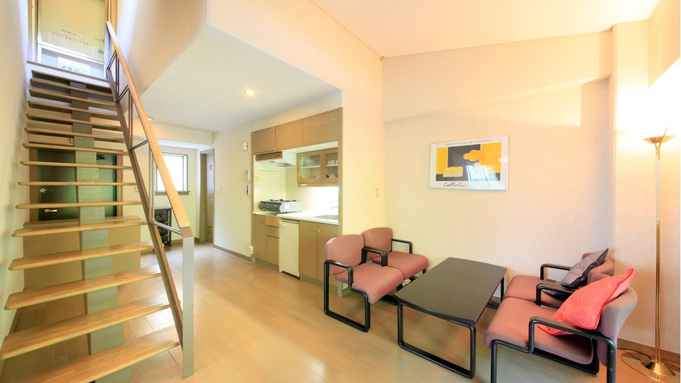 Un intérieur moderne avec un escalier, un coin repas comprenant une table et des chaises, et une cuisine en arrière-plan.