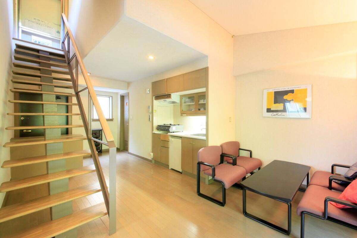 A modern interior with a staircase, a dining area with a table and chairs, and a kitchen in the background.