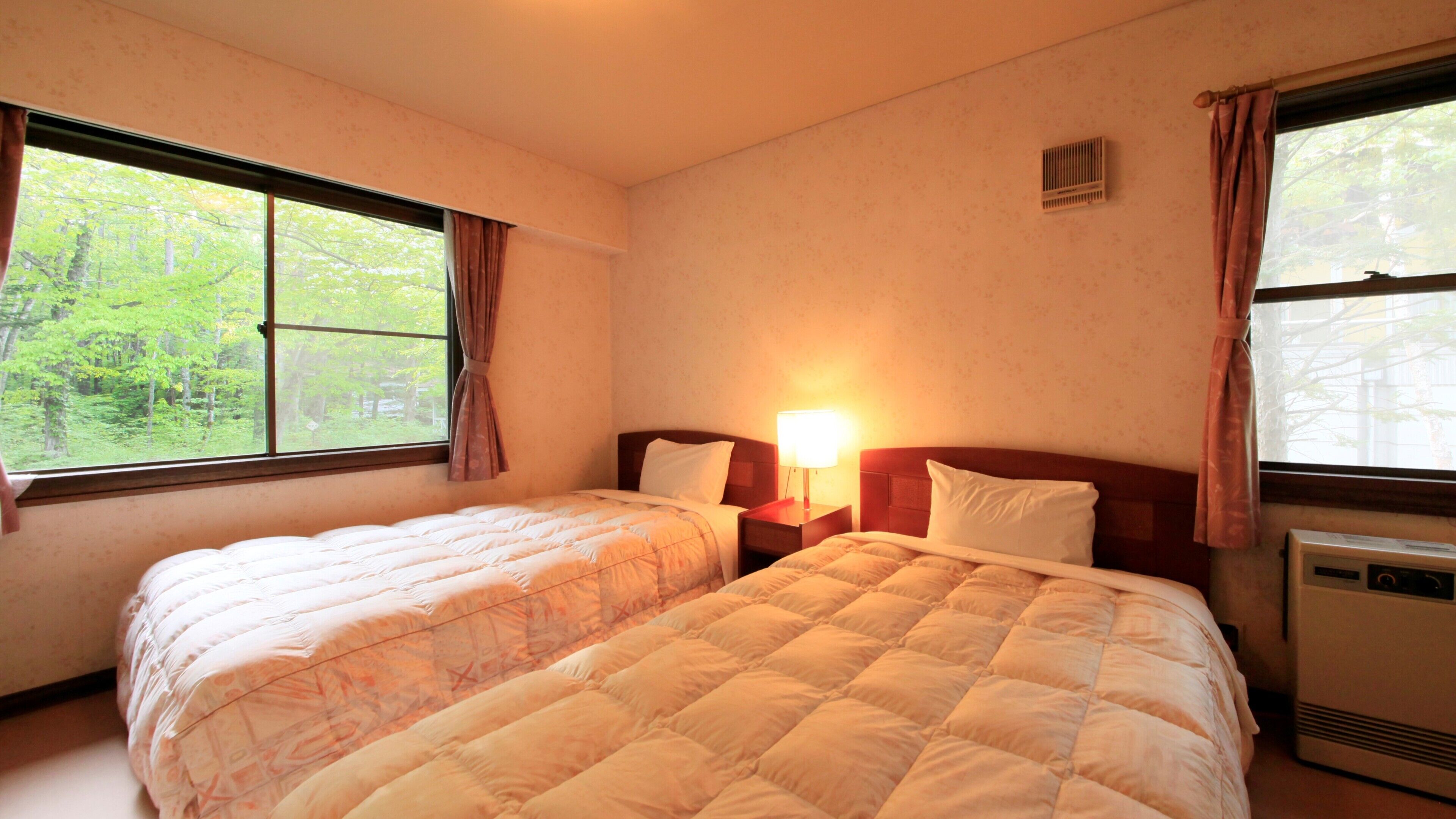 A hotel room with two beds, a nightstand with a lamp, a heater, and a window with curtains.