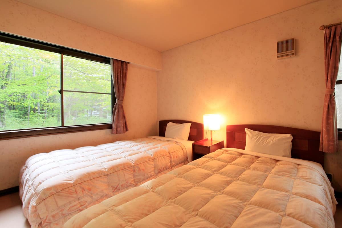 Une chambre d’hôtel avec deux lits, une table de chevet avec une lampe, un radiateur et une fenêtre avec des rideaux.