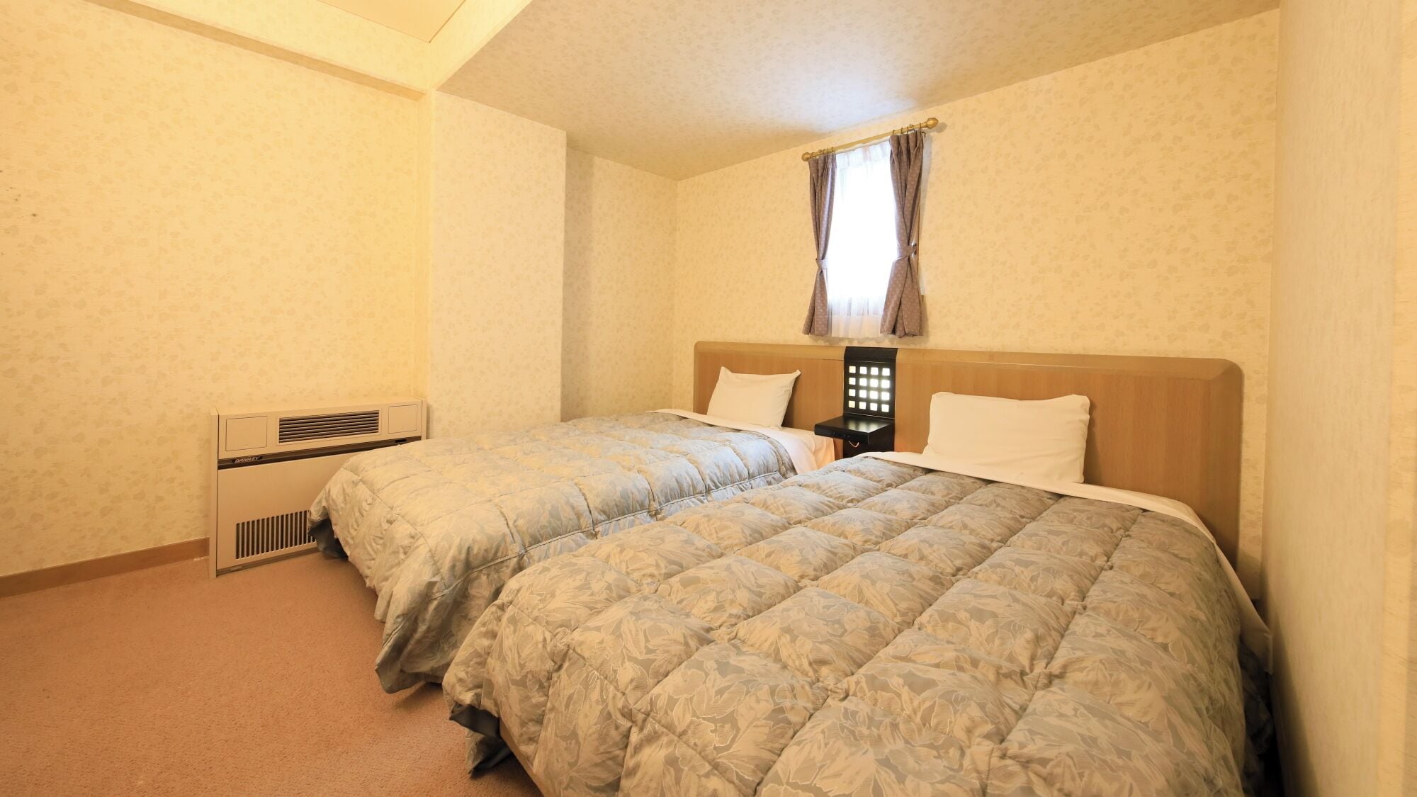 A bedroom with two beds, a window with curtains, a heater, and a nightstand.