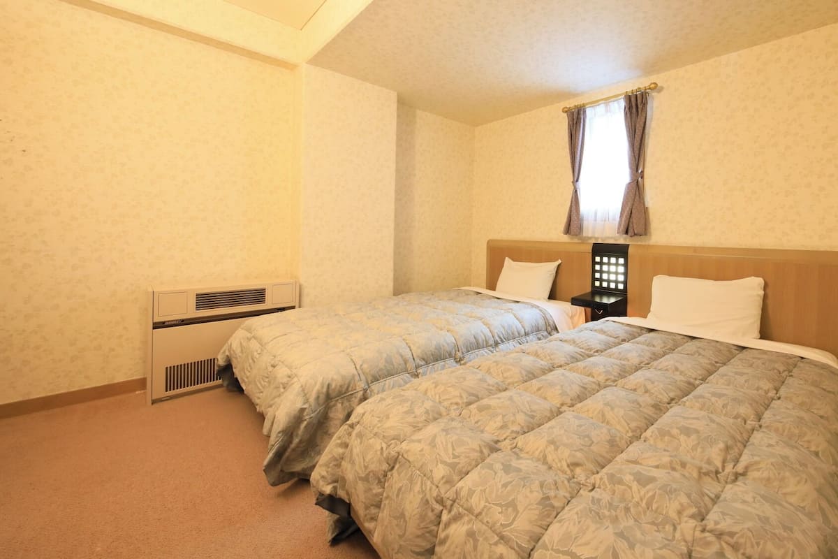 Une chambre avec deux lits, une fenêtre avec des rideaux, un radiateur et une table de chevet.