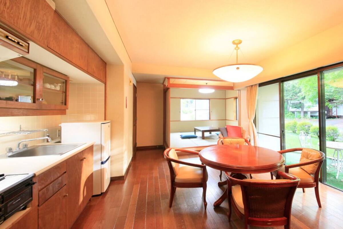A modern kitchen with a dining area, wooden cabinets, and a large window with a view of the garden.