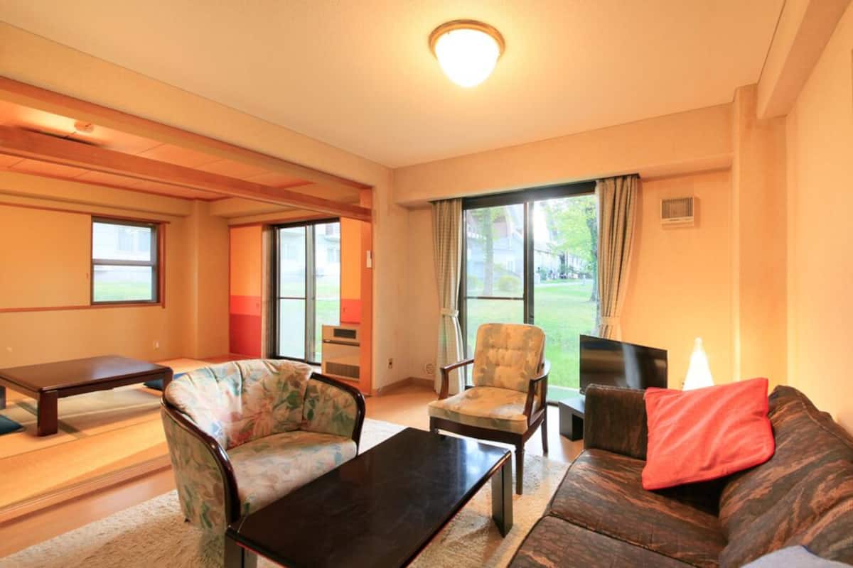 A living room with a sofa, armchair, coffee table, and a dining table.