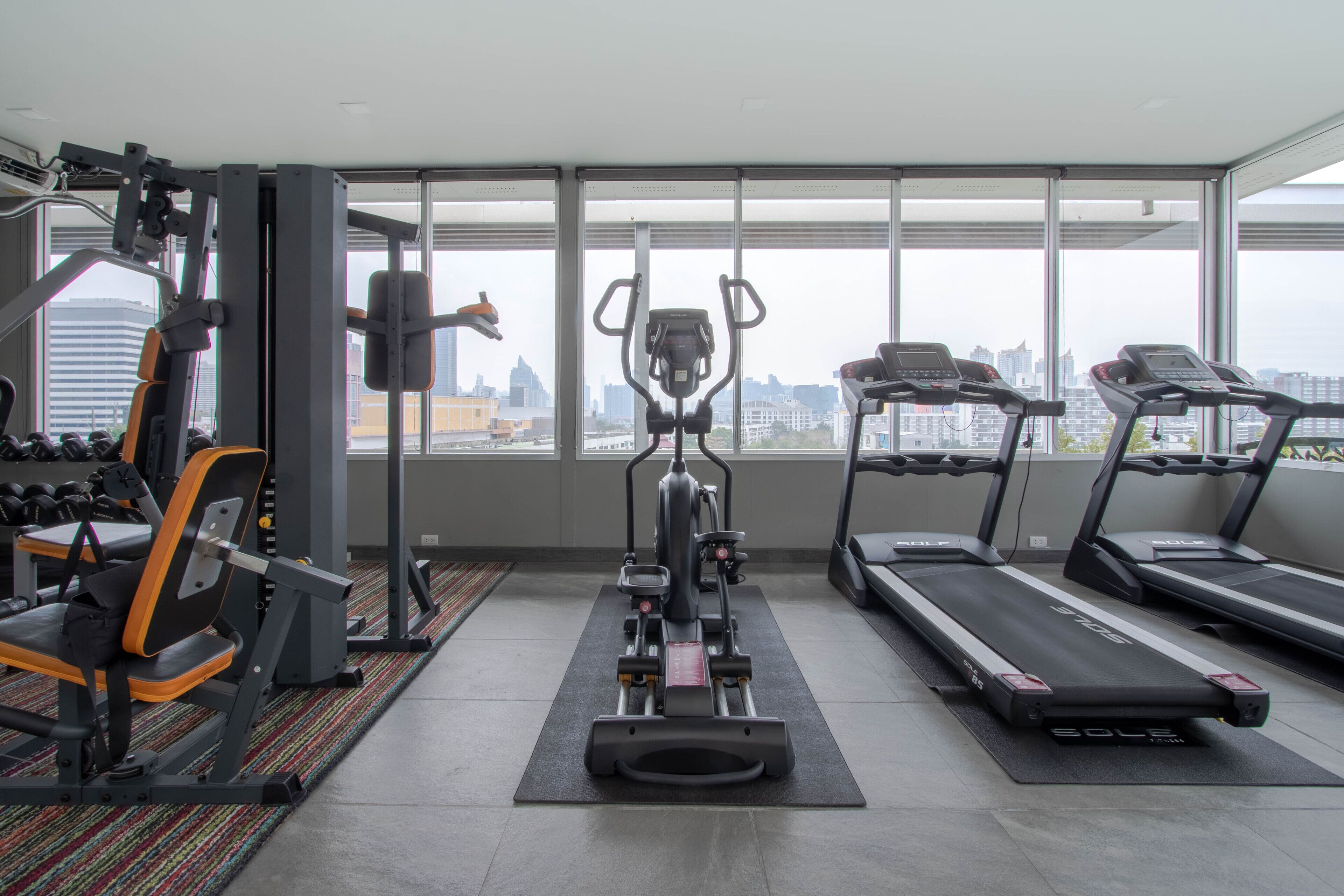 A gym with exercise equipment, a treadmill, and a city view through large windows.