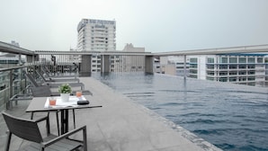 Zona de piscina en la azotea con mesa y sillas, rodeada por una barandilla y vistas a un paisaje urbano.