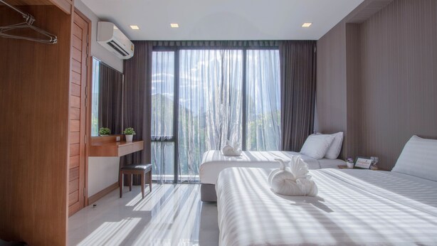 Habitación de hotel con dos camas, un armario de madera, una mesita con una planta y un ventanal con cortinas.