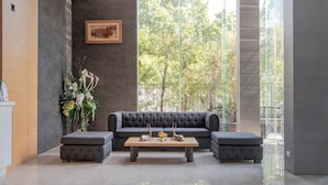Un vestíbulo moderno con un sofá gris, dos otomanas a juego, una mesa de centro de madera y un ventanal con vistas a árboles.