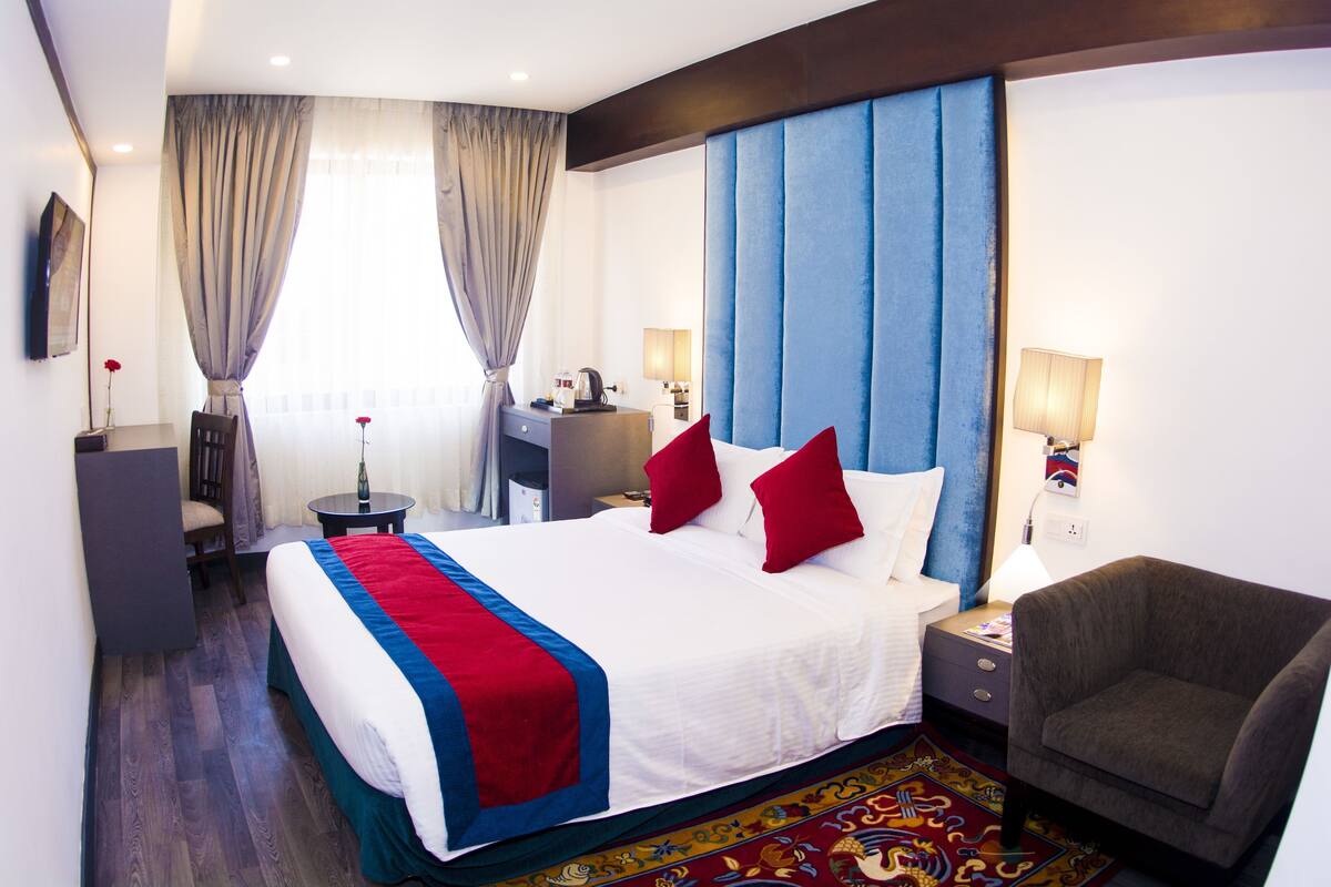 A hotel room with a large bed, a desk, a chair, and a nightstand.