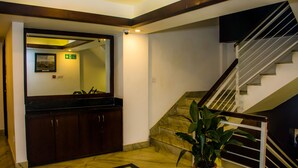 Un vestíbulo de hotel con piso de mármol, una mesa de recepción, un espejo grande y una escalera.