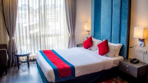 Habitación de hotel con una cama grande, una mesita de noche con lámpara, una pequeña mesa y una silla.