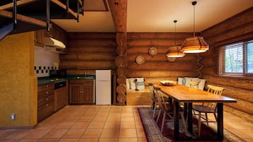Interior de una cabaña de madera con cocina, comedor y un ventanal grande.