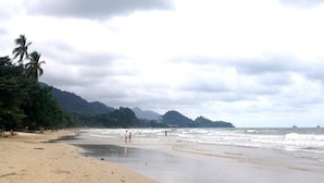 A beach with a sandy shore, palm trees, and a hilly landscape in the background. - The Erawan Koh Chang (Ko Chang)