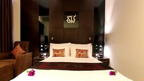 A hotel room with a large bed, two bedside lamps, a brown leather armchair, and a decorative wall piece. - The Erawan Koh Chang (Ko Chang)