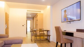 A modern living room with a sofa, a coffee table, a TV mounted on the wall, and a dining area with a table and chairs. - The Erawan Koh Chang (Ko Chang)