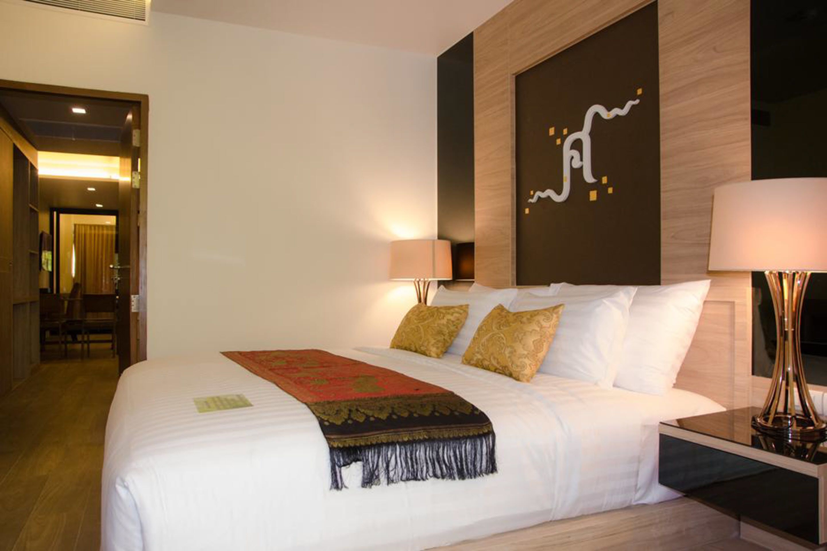 Una habitación de hotel con una cama bien hecha, una obra de arte grande en la pared y una lámpara en la mesita de noche.