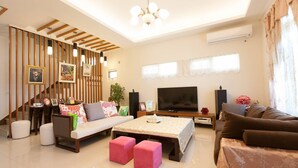 Uma sala de estar moderna com um sofá, pufes, uma mesa de centro, uma televisão e uma escada com corrimão.