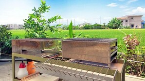 Duas grelhas de cozinha ao ar livre com uma grade de metal em primeiro plano, com um campo verde e edifícios residenciais ao fundo.