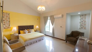 Quarto de hotel com cama, mesas de cabeceira, uma cadeira, escrivaninha e um candelabro.