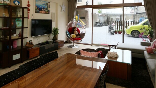 A modern living room with a wooden dining table, a TV, and a large window with a view of the street. - Luckystar B&B (Luodong)