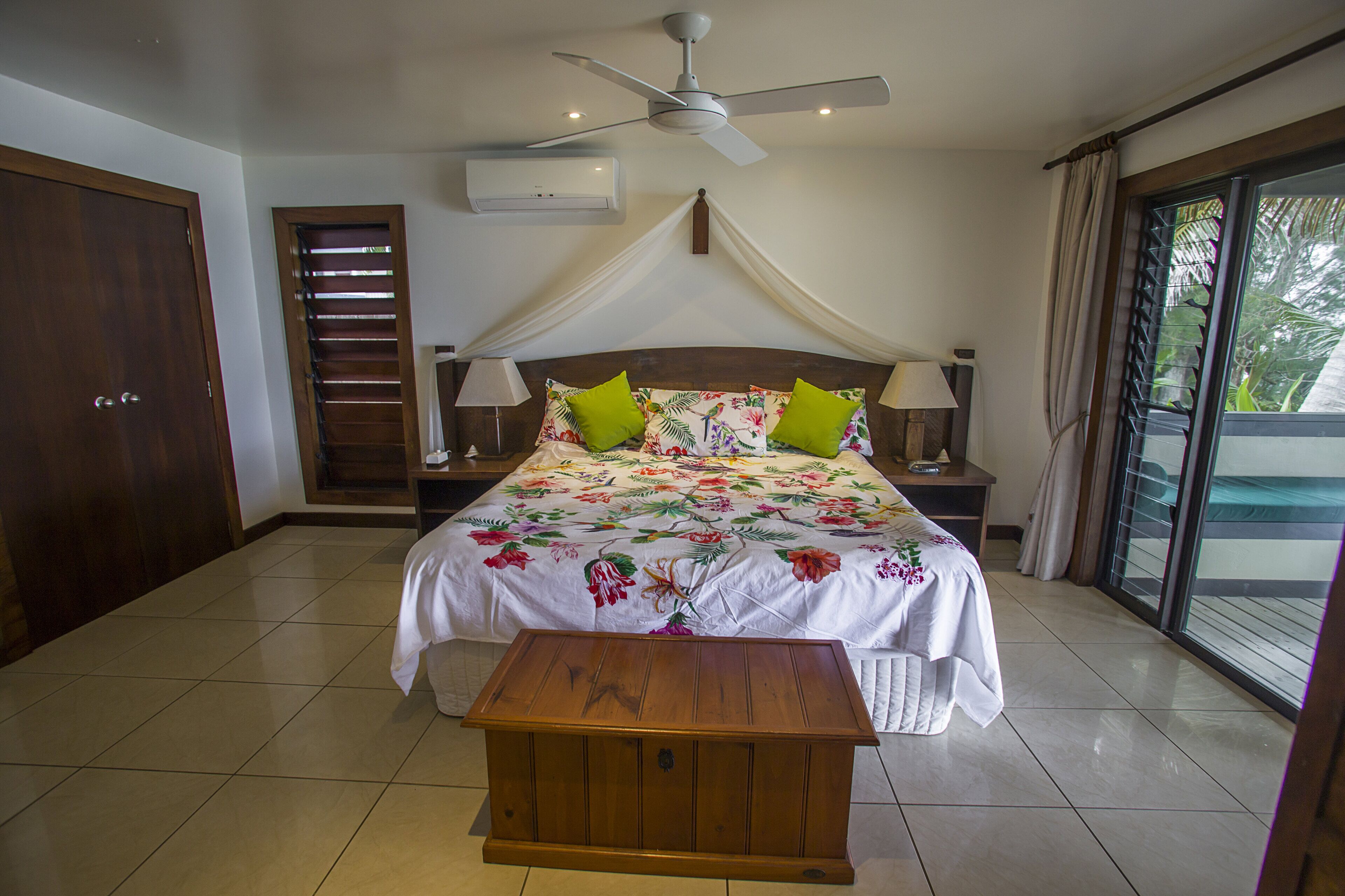 A bedroom with a bed, a ceiling fan, a bedside table, and a window with curtains.