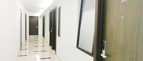A hallway with white walls, a tiled floor, and doors numbered 305.