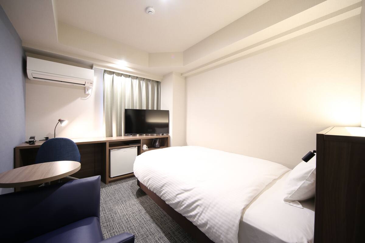 A hotel room with a bed, a desk with a chair, a television, and a small table.