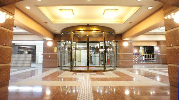 Una puerta giratoria con cerramiento de vidrio, que da acceso a un vestíbulo con suelo de baldosas e iluminación empotrada en el techo.