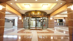 A revolving door with a glass enclosure, leading to a lobby area with a tiled floor and a ceiling with recessed lighting. - Hotel Kajigaya Plaza (Kawasaki)