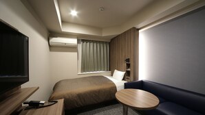 Una habitación de hotel moderna con cama, una mesita, televisor y ventana con cortinas.