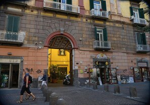 A building with a large arched entrance, a shop with a sign reading "Lecciose," and a street with bollards and pedestrians. - B&B Cuore di Napoli (Naples)