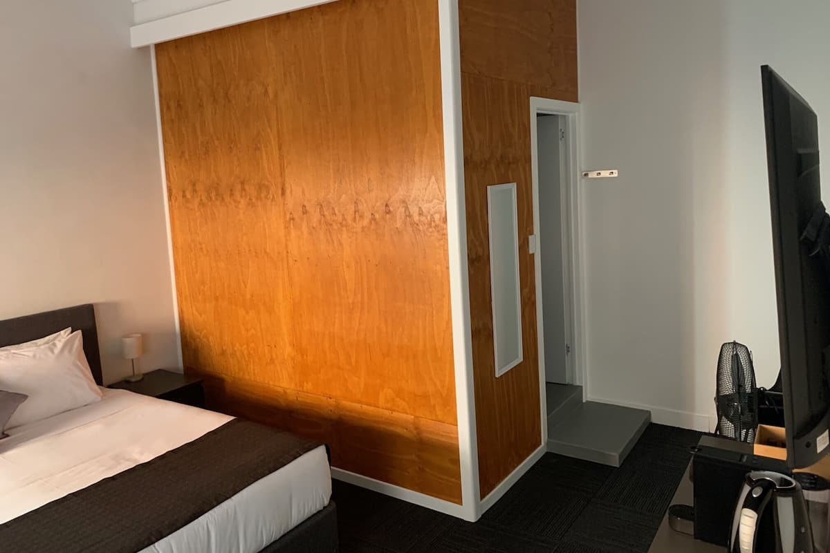 Quarto de hotel com cama, divisória de madeira, televisão e mesa com cadeira.