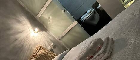 A hotel room with a neatly made bed, a large window with a view, and a wall-mounted light fixture.
