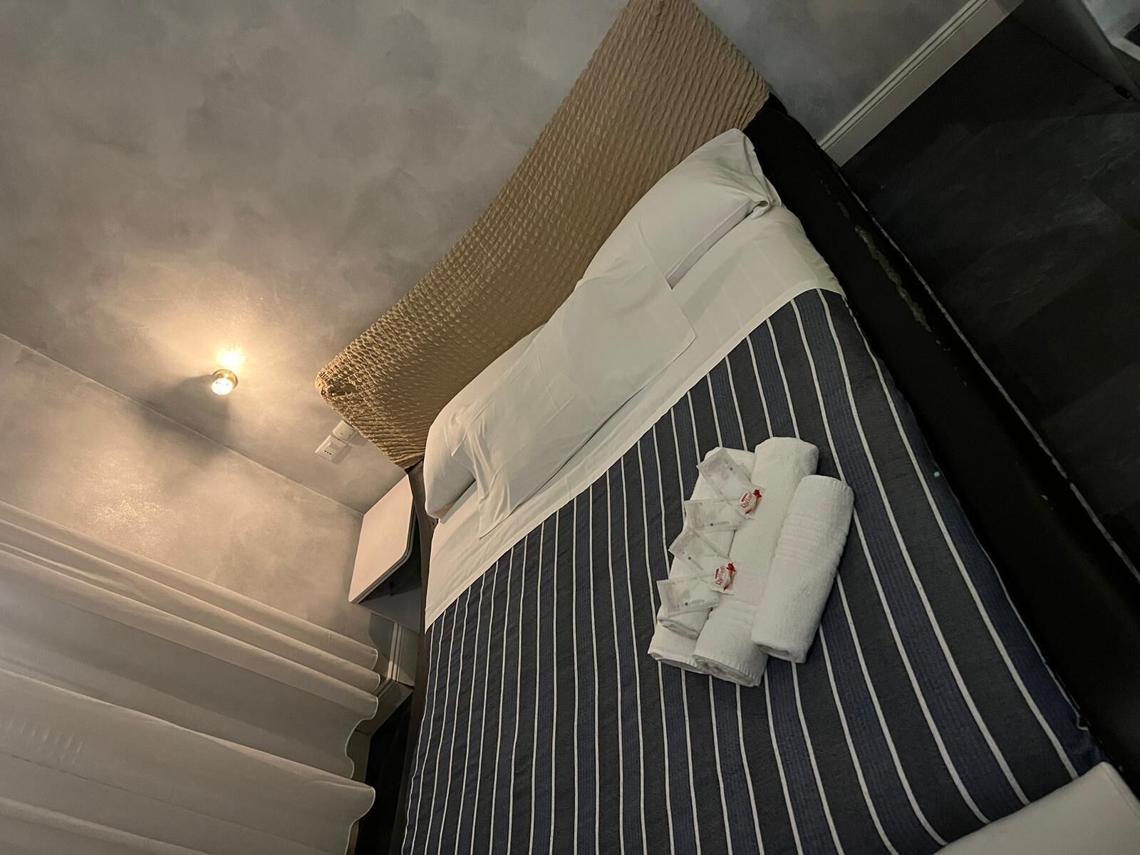 Una habitación de hotel con una cama a rayas, un cabecero tejido y toallas dobladas con cuidado.