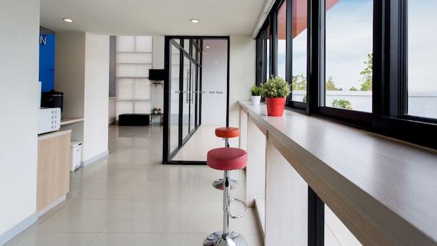 A modern hotel corridor with a bar area featuring a red stool and potted plants. - Hop Inn Rayong (Rayong)