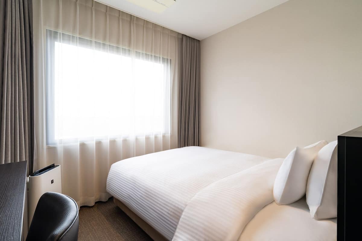 A hotel room with a large bed, a desk, and a chair.