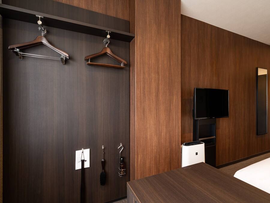 A hotel room with a dark wood wardrobe, a bed, a TV, and a mirror.