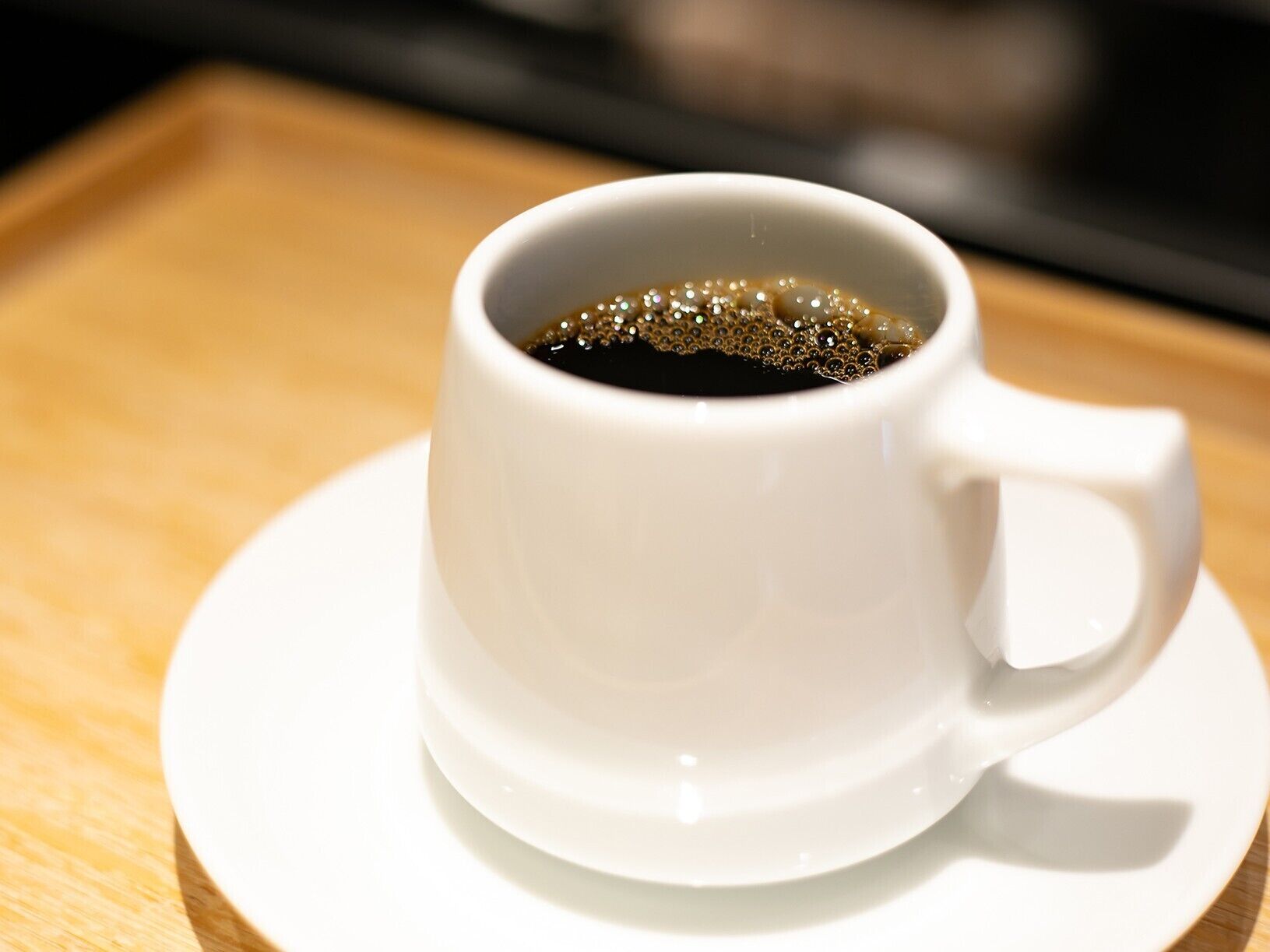 A white cup of coffee on a white saucer.