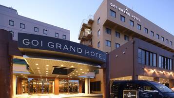 Entrada del GOI GRAND HOTEL con diseño moderno, que destaca un letrero llamativo, una puerta de cristal y un estacionamiento con una camioneta.