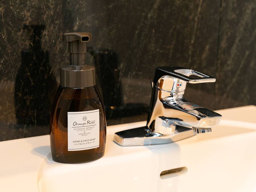 A bottle of Orange Rose hand and face soap next to a modern faucet on a white sink.