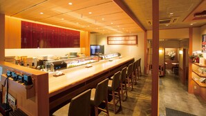 Una barra larga de sushi, zona de asientos y decoración tradicional japonesa.