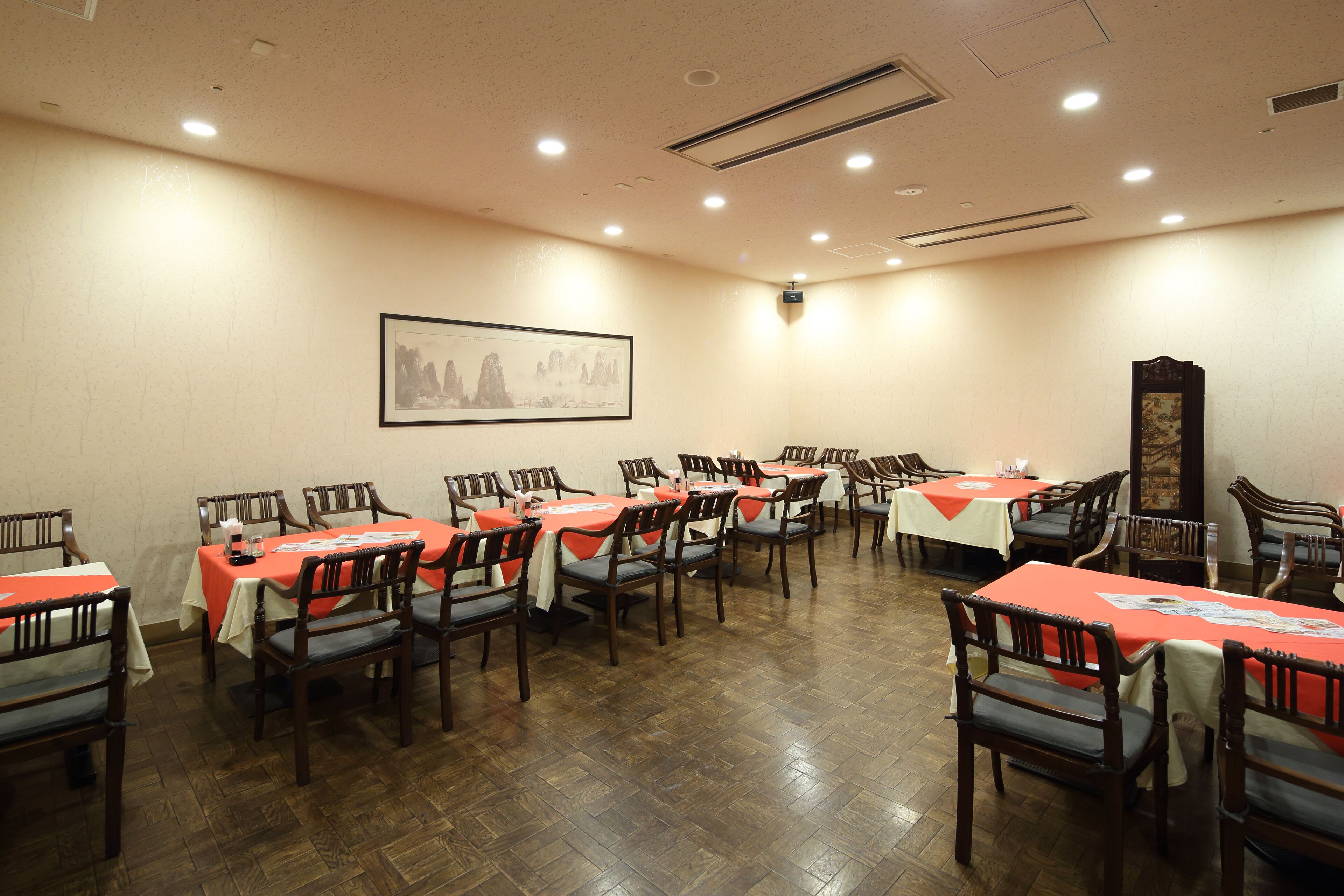 A conference room with multiple tables and chairs, a framed picture on the wall, and a wooden floor.