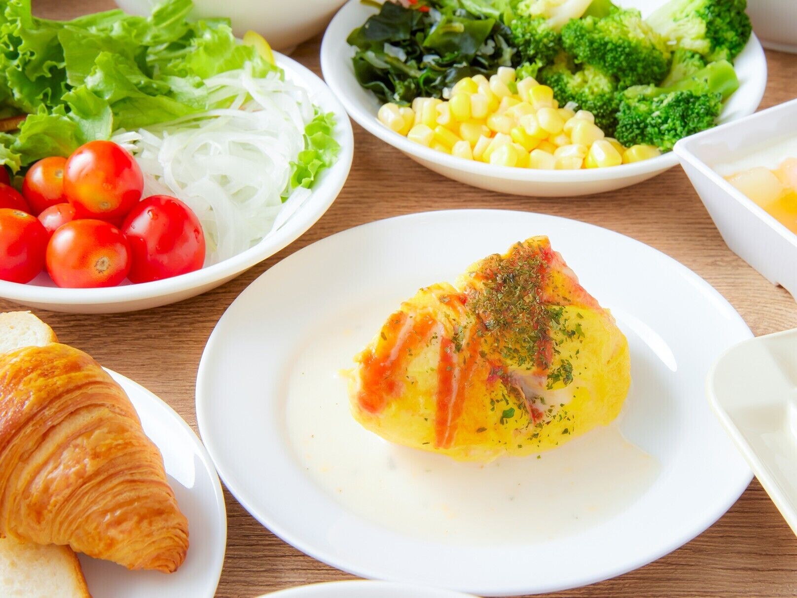A meal with a croissant, a plate of fish, and various vegetables.