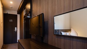 Una habitación de hotel con pared de paneles de madera, un televisor de pantalla plana montado sobre un escritorio de madera y un espejo grande que refleja parte de la habitación.