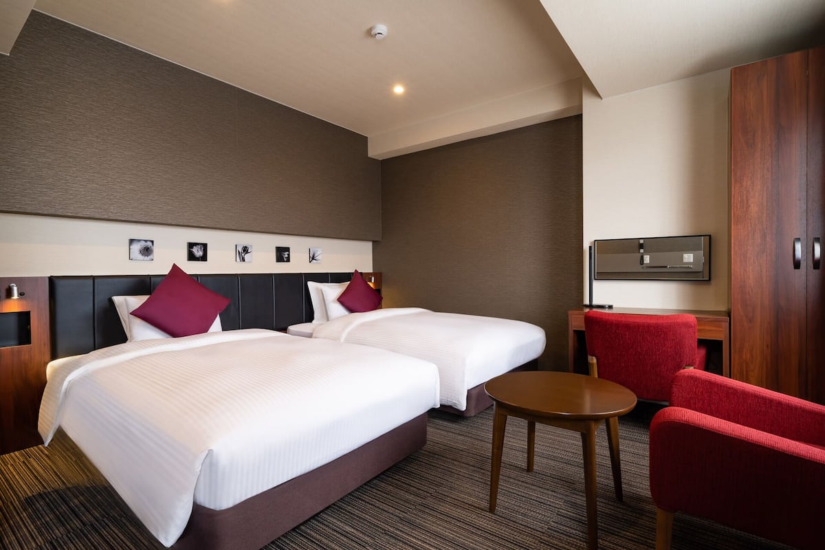 A hotel room with two beds, a desk, a chair, and a flat-screen TV.